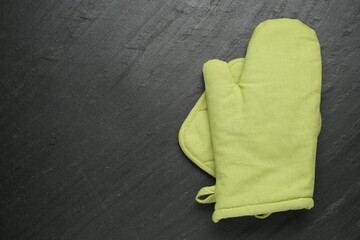 Green oven glove and potholder on dark textured table, top view. Space for text