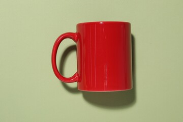 Red mug on light green background, top view. Mockup for design