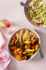 A nutritious breakfast showcases a bowl of quinoa accompanied by vibrant baked sweet potatoes, carrots, zucchini, beans, and turmeric chicken, paired with a fresh salad on the side