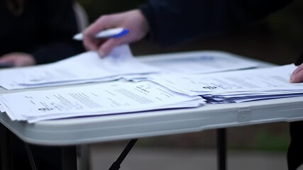 Papers stacked on a table with hands flipping through them, outside setting