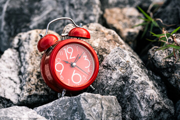Vintage red alarm clock on rugged stones outdoor photography natural light capturing time's essence