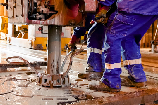 Driller's assistants near the drilling table on oil drilling platform soiled the overalls with drilling fluid.