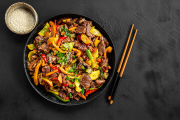 Beef stir fry in a frying pan top view, Asian meat with vegetables on a black background top view