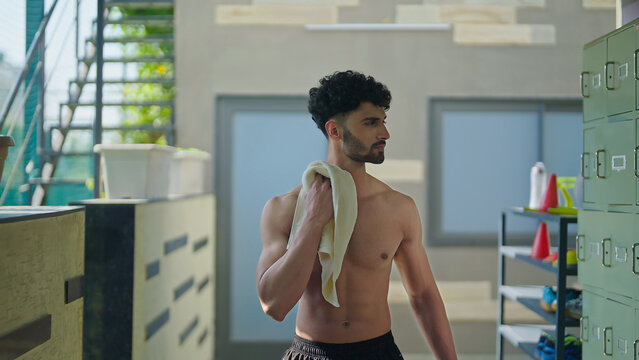 Indian young adult man guy walking indoor changing room hold towel wipe off sweat after morning fitness workout Asian relax sports male well being boy take break time at inside campus - Powered by Adobe