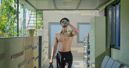 Indian gen z young adult male man standing indoor hall way hold bottle drink fresh water Asian well being boy guy take break after sports workout match game spend time inside corridor area