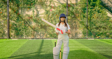 Indian young adult gen z sports woman lady standing at outdoor ground day wear white uniform and helmet look camera. Asian female girl player hold bat staring cam play do casual pose
