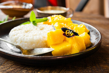 Thai mango sticky rice with coconut milk, garnished with edible flowers close up