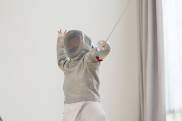 Asian boy in fencing costume with fencing sports mask and holding sword for practicing and training in gym. Teen boy fencer athlete fencing training in classroom