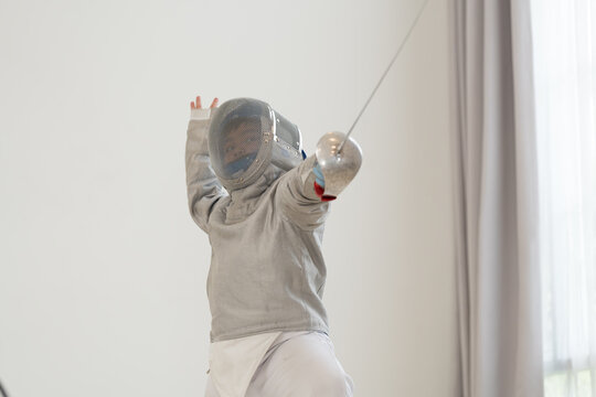 Asian boy in fencing costume with fencing sports mask and holding sword for practicing and training in gym. Teen boy fencer athlete fencing training in classroom