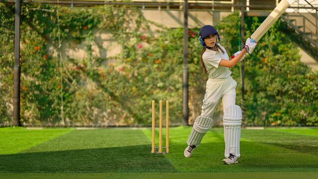Indian young adult gen z sports woman lady standing hold bat play learn cricket match do practice to hit ball at garden angry teen female girl player wear white uniform leg guard hand gloves day time
