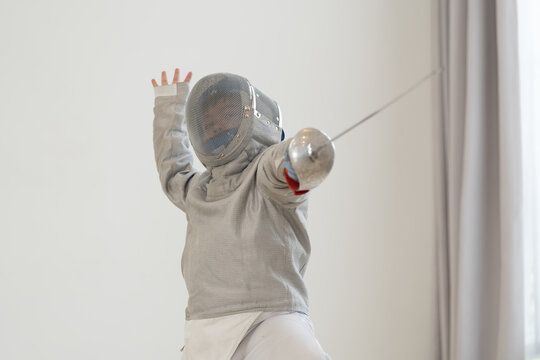 Asian boy in fencing costume with fencing sports mask and holding sword for practicing and training in gym. Teen boy fencer athlete fencing training in classroom