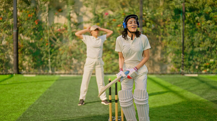 Indian gen z young adult woman lady wear hand gloves white dress leg guard helmet day time cricket player sports teen female girl hold bat play casual match game hit ball do batting at ground place