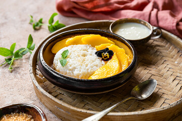 Thai mango sticky rice with coconut milk, garnished with edible flowers on light table