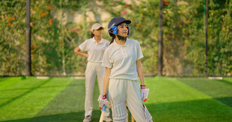 Indian gen z young adult woman lady wear hand gloves white dress leg guard helmet day time cricket player sports teen female girl hold bat play casual match game hit ball do batting at ground place