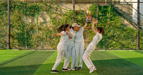 Indian young adult gen z sports woman lady group win match held award in hand raise up enjoy day time happy female team cheering have fun joy do jump hug shout loud scream yes at play ground place