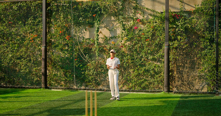 Indian young adult gen z bowler woman lady standing at match ground wear white uniform with cap. Asian teen age female girl running play cricket learn game do practice to hit wicket throw ball place