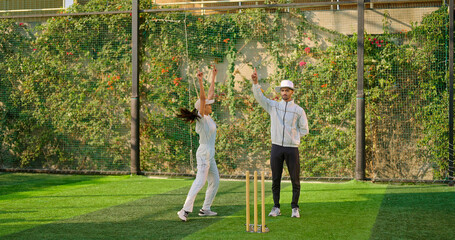 Indian young adult gen z bowler woman standing outdoor match play ground wear uniform cap. Asian...