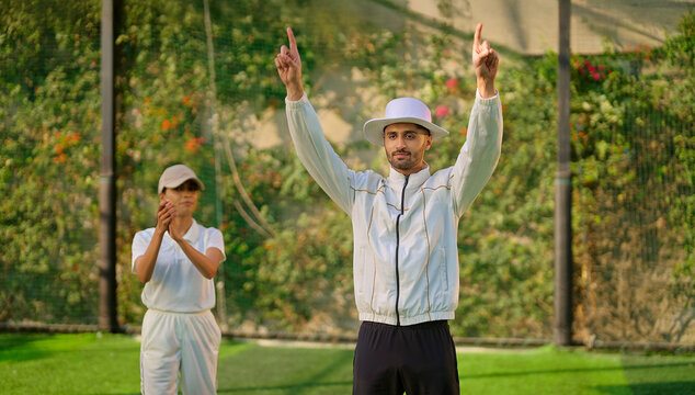 Indian young adult gen z bowler woman standing outdoor match play ground wear uniform cap asian female lady throwing ball do practice clap hand umpire man show six run two hands signal