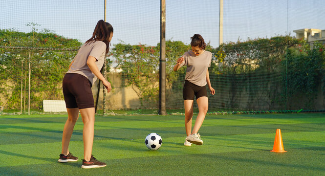 Indian asian happy young adult gen z girl group of sports woman playing football outdoor yard smiling female lady players game kicking soccer ball team have fun joy give high five outside ground place