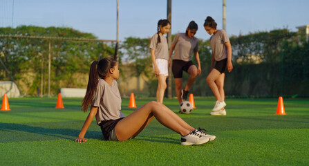 Fototapeta premium Indian young adult woman lady group team play football enjoy day have fun joy outdoor place tired upset sad gen z female girl player sitting on ground take rest time relax break after sport game