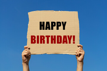 Happy birthday text on cardboard paper holding by a woman's hand with blue sky background