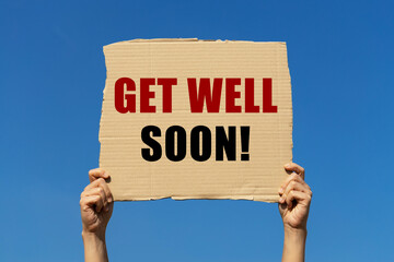 Get well soon text on cardboard paper holding by a woman's hand with blue sky background