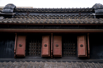 Traditional kura storehouse in Kawagoe, Japan, featuring black kawara tiled roof, wooden shuttered windows, and preserved historic architecture. © Denise