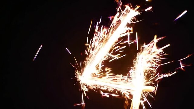 Close-Up Shot of Sparkler Stick Shaped into the Number Four Emitting Bright Sparks Against Black