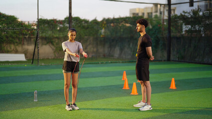 Obraz premium Indian young adult gen z woman lady jump on skip rope work out for weight lose. fit man gym trainer male guy coach watch sports female girl do daily health care learn good habit game garden place area
