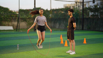 Indian young adult gen z woman lady jump on skip rope work out for weight lose. fit man gym trainer...