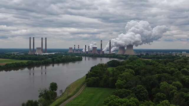 Industrial power generation facilities situated in rural Ohio locale, encircled by farmland and forests, captured from stationary aerial drone perspective