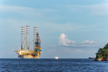 Offshore oil rig platform near tropical coastline under cloudy sky