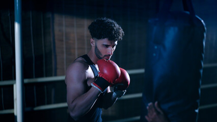 Indian young adult gen z angry fit boxer man guy wear gloves do hand fist boxing punch beat on bag...