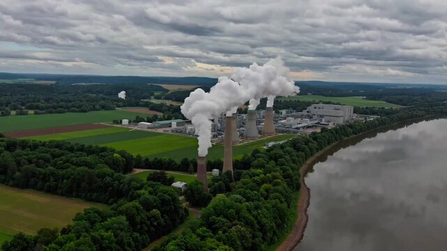 Industrial power generation facilities situated in rural Ohio locale, encircled by farmland and forests, captured from stationary aerial drone perspective