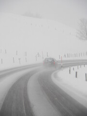 Car is driving down a snowy road with a white line painted on the road