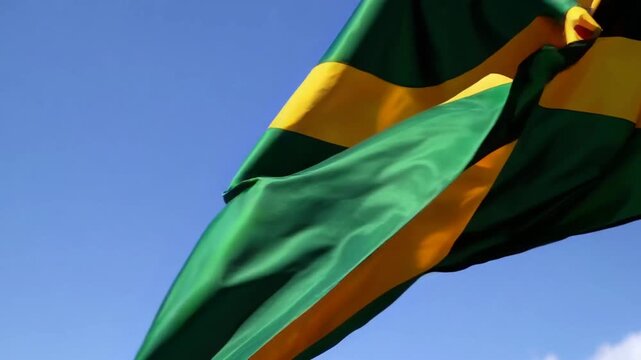 The official symbolic banner of the nation Jamaica moving gently in the breeze against solid azure sky