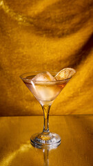Golden cocktail with ice cube and dried citrus slice on reflective background. Concept of bar advertising, luxury beverage, celebration, nightlife and premium alcohol branding.
