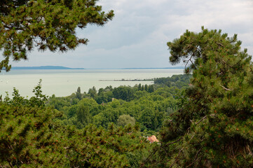 Overlooking the beautiful Lake Balaton with lush green trees and a cloudy sky.