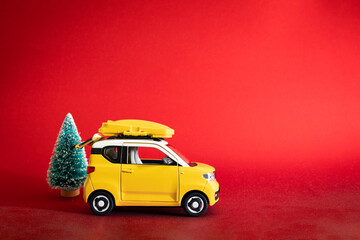Yellow car with roof rack, open trunk, and Christmas tree on red background. Concepts: buying Christmas trees