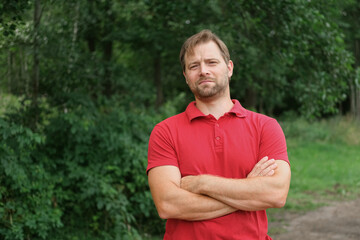 Portrait of handsome young man in a red t-shirt outdoors. Male with fair hair and beard feel happy,...