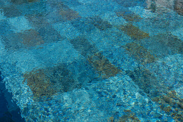 Zoom sur le fond d’une piscine en carrelage avec des carreaux multicolores formant un jeu de textures et de nuances.