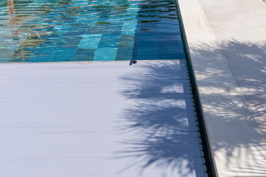 Zoom sur le fond d&rsquo;une piscine en carrelage avec des carreaux multicolores formant un jeu de textures et de nuances avec une b&acirc;che &eacute;lectrique qui se referme.