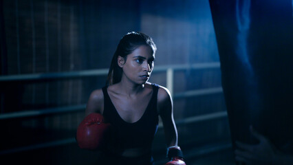 Indian young adult gen z angry fit boxer woman lady wear gloves do hand fist boxing punch beat on...