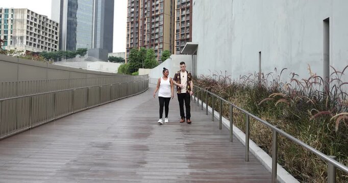 Asian Indian adult woman and Caucasian adult man urban rooftop outdoor casual pose walk talk activity friend colleague various expression - Powered by Adobe