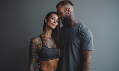 Fitness couple with tattoos sharing a loving moment against a neutral background in a stylish urban setting during a casual photoshoot