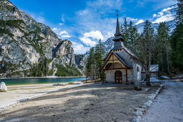 Scenic Lago di Braies, Italy, featuring its quaint chapel, traditional wooden rowboats, and peaceful shoreline backed by dense trees. A beautiful Dolomite lake view.
