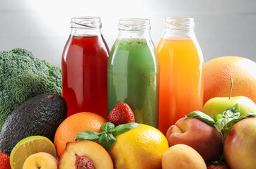 Tasty juices in glass bottles, fresh ingredients and basil against light grey background, closeup