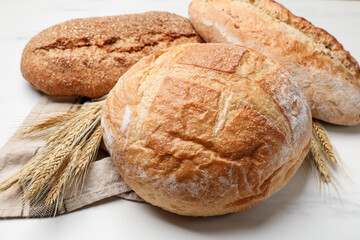 Different types of bread and wheat spikes on white marble table, closeup