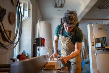 Carpenter maintain concentration on shaping wooden beam with jointer machine in workshop. Master...