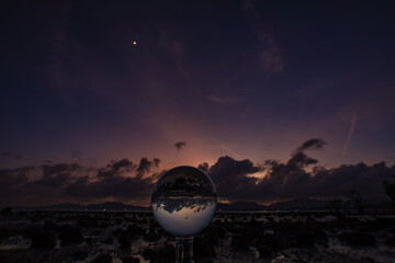  A mesmerizing sunset over a rocky shoreline captured through a glass crystal ball, creating a...